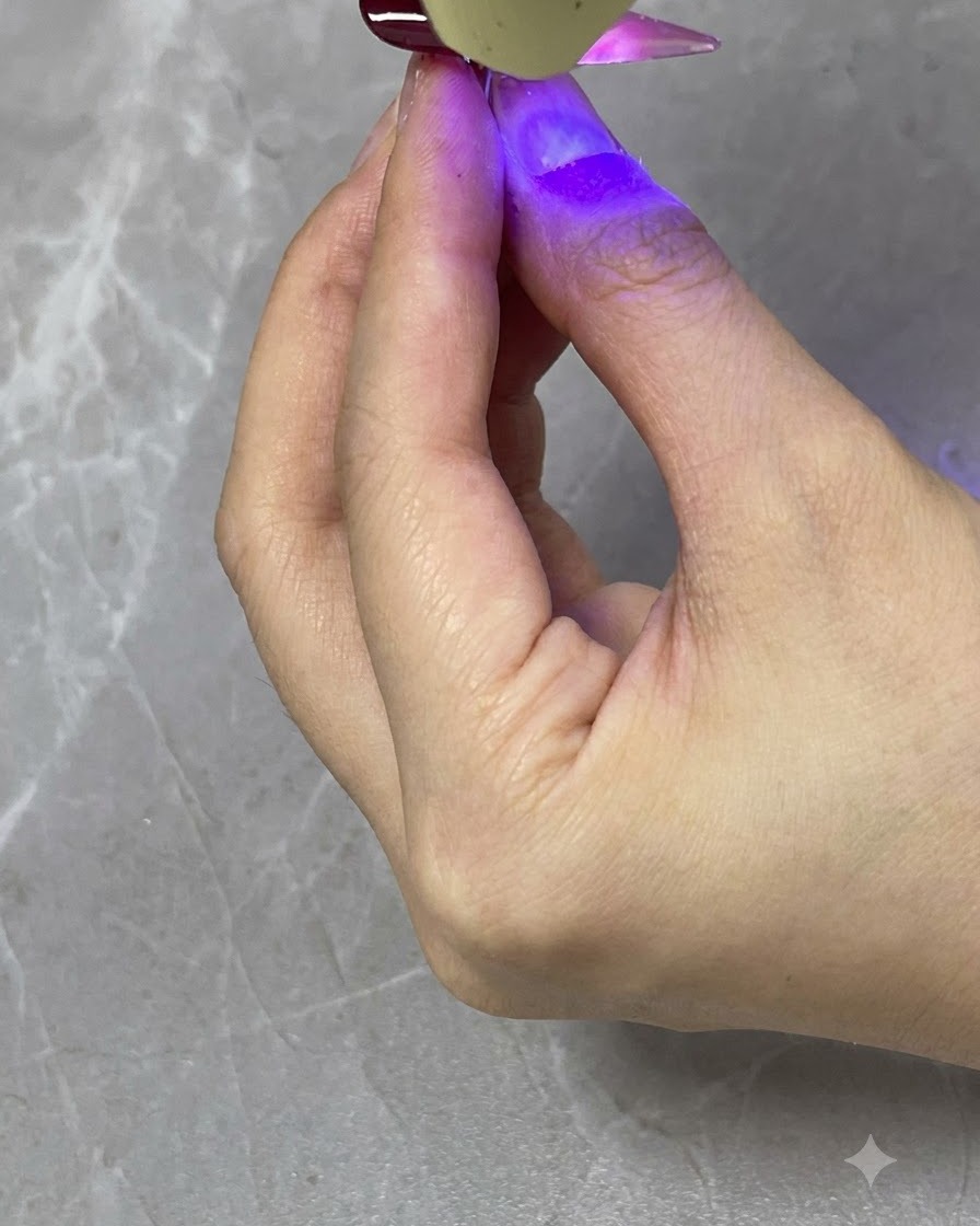 Eine tragbare UV-/LED-Lampe härtet eine transluzente rote Farbverlaufsschicht auf einem fertigen Nagel aus.