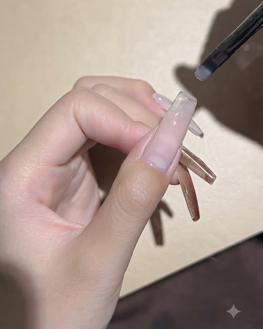 Un pequeño pincel de gel aplicando una capa suave de gel base transparente sobre una placa de uña extendida.