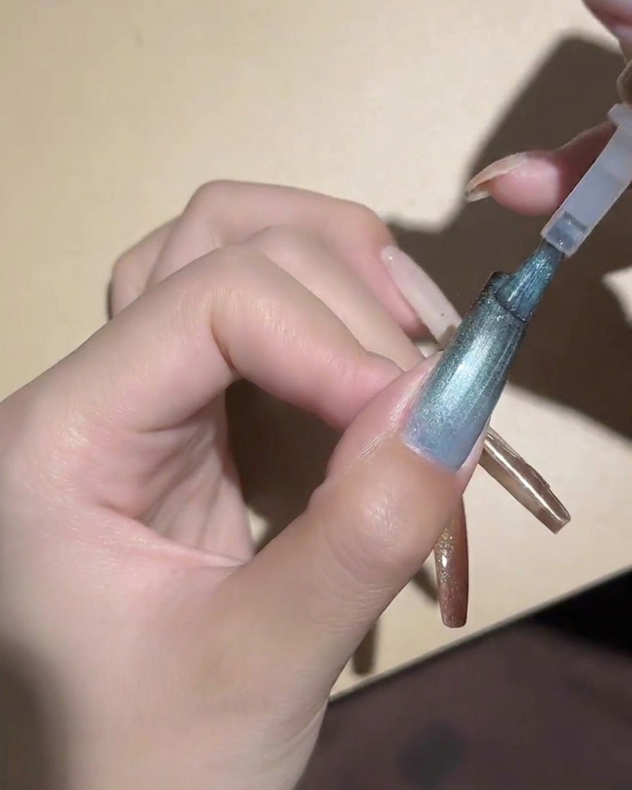 Un imán cilíndrico sostenido cerca de una uña azul de ojo de gato para magnetizar las partículas.