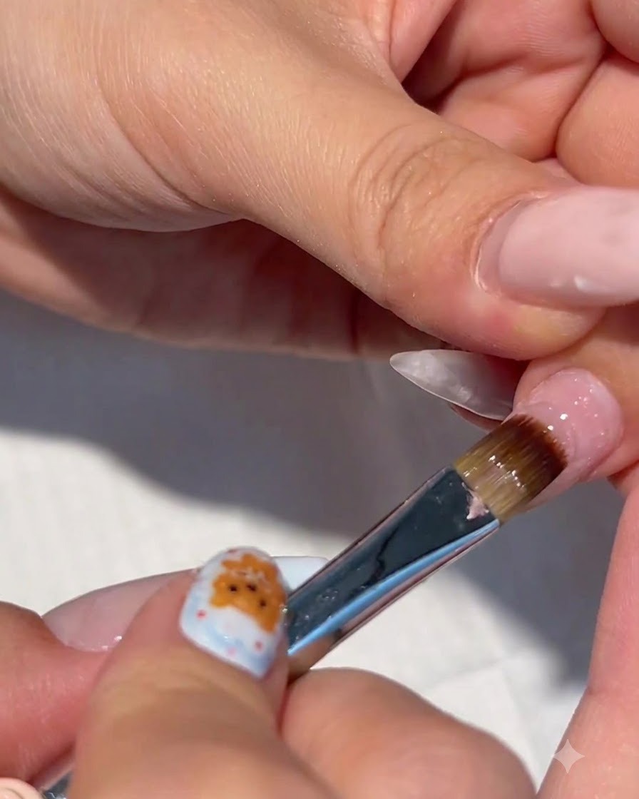 Un primer plano de un pincel de uñas aplicando gel de construcción transparente sobre una uña previamente preparada.