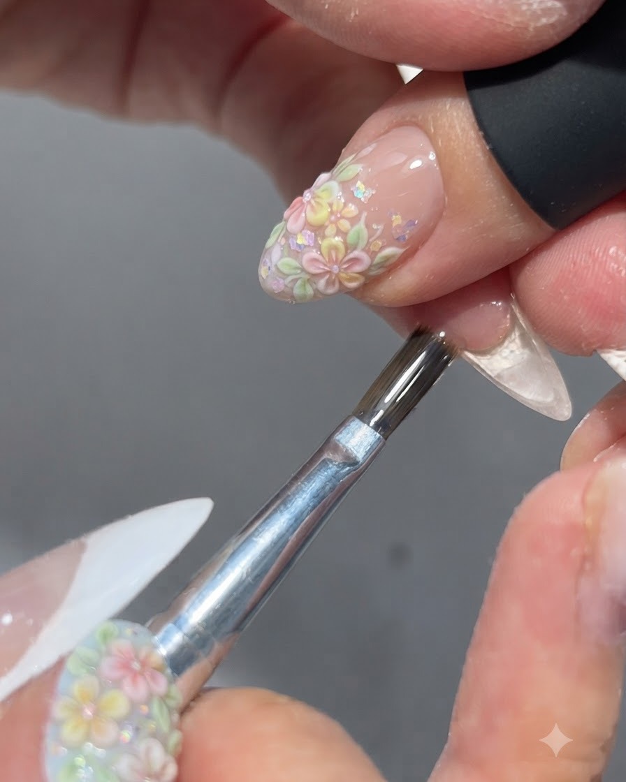 Un pincel aplicando una capa superior brillante sobre un diseño de uñas floral completado.