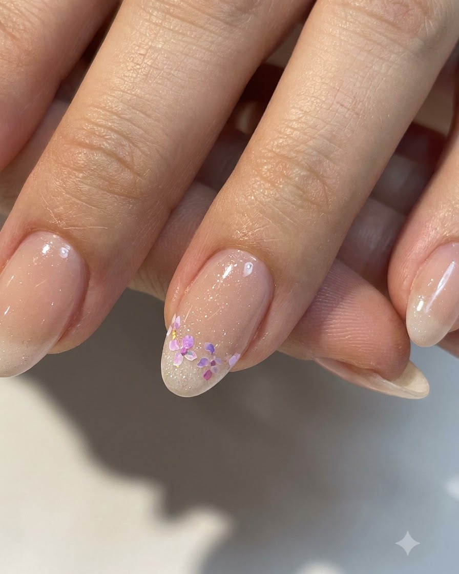 Un primer plano de un pequeño arte de uñas floral completado sobre una base nude brillante con detalles refinados.