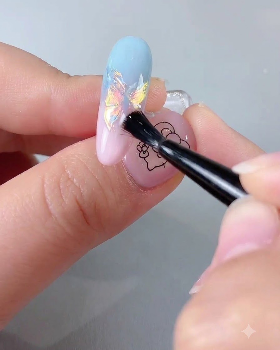 Un pincel aplicando un top coat sellador transparente sobre una extensión de uña con acabado cromado iridiscente.