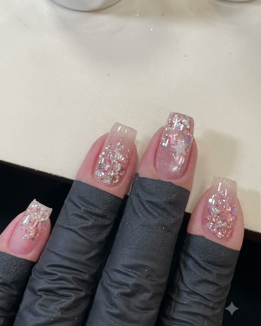 Una toma cenital de cuatro uñas manicuradas decoradas con lentejuelas rosas brillantes y el contorno de una estrella.