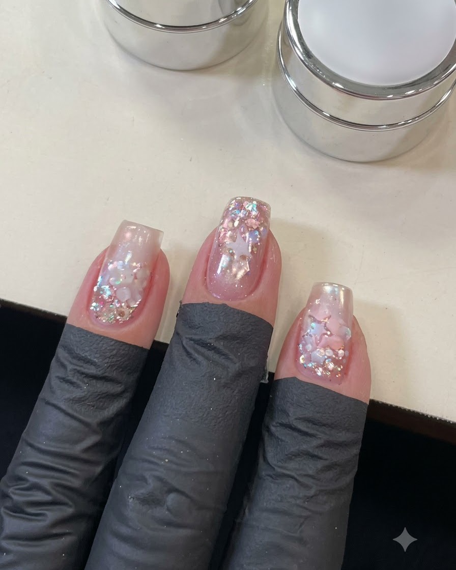 Una vista de cerca de una mano aplicando la capa superior sobre el detallado arte de uñas con estrellas y lentejuelas.