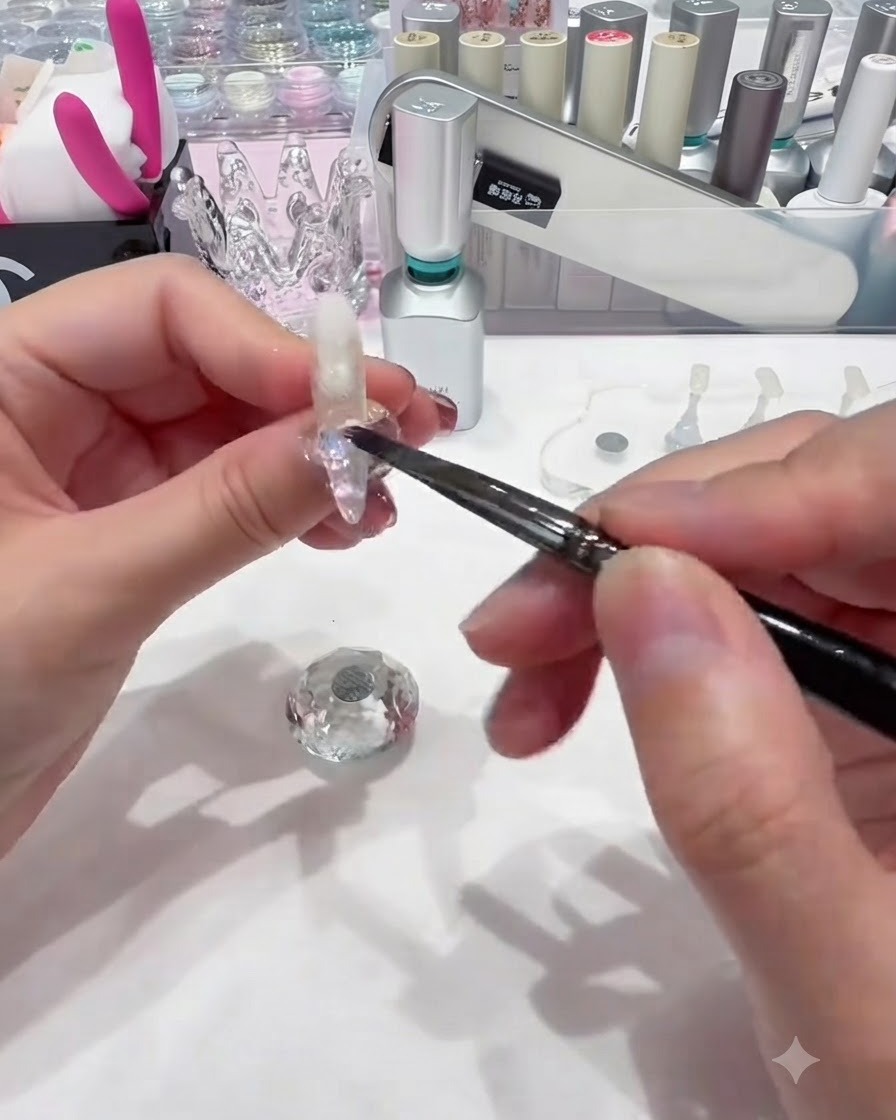 Un pequeño pincel de uñas dejando caer lentejuelas circulares de colores sobre el gel base húmedo cerca de la base de la uña.
