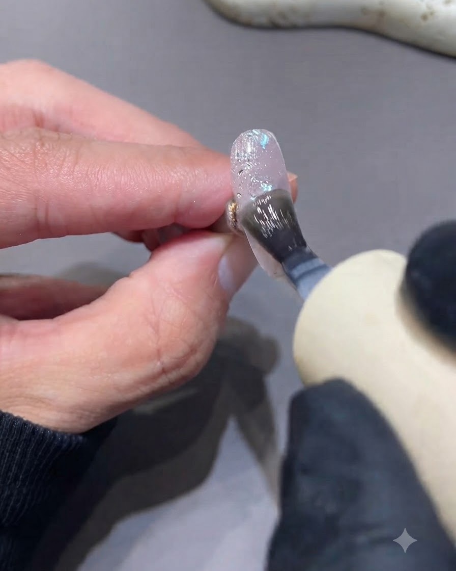 Un pincel aplicando top coat mate sobre una uña texturizada con purpurina y lentejuelas.