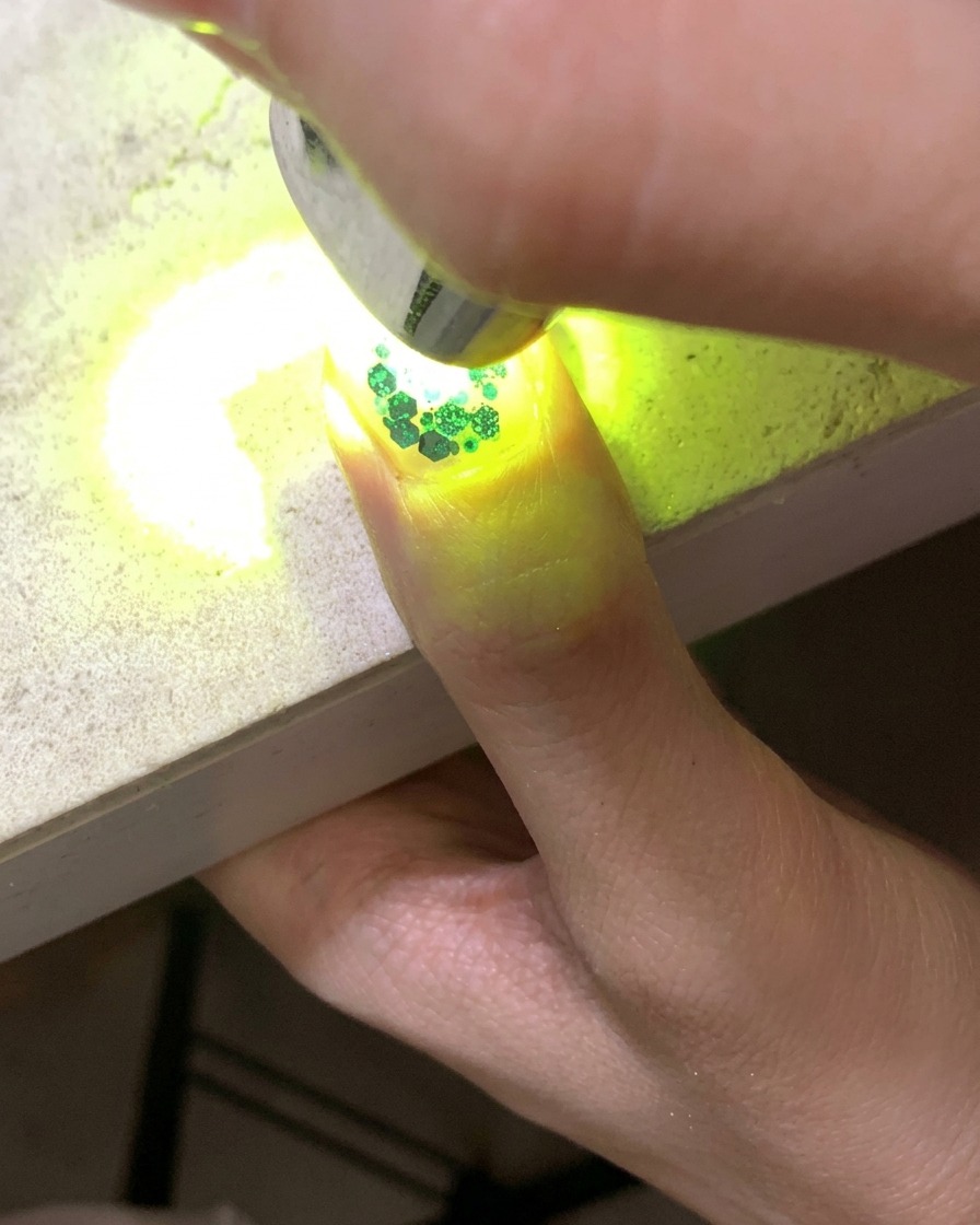 Una minilámpara UV curando una uña adornada con purpurina y lentejuelas de estrellas huecas.