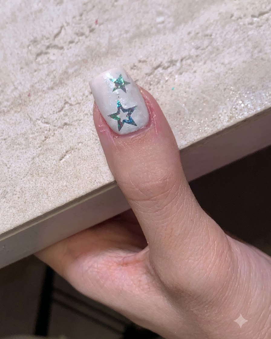 Una uña con pegatinas de estrellas colocada bajo una pequeña lámpara LED portátil para su curado.