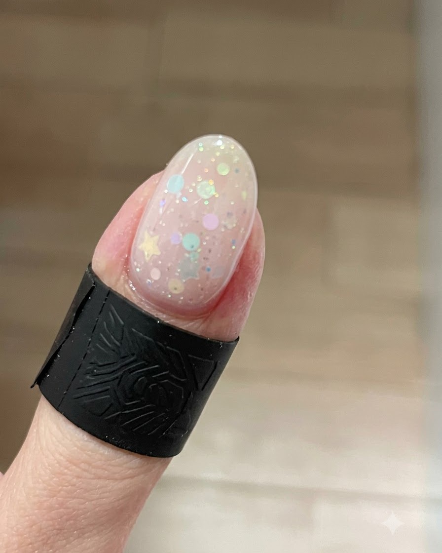 Primer plano de una uña que muestra un efecto ojo de gato brillante concentrado en la punta, sobre glitters de estrellas.