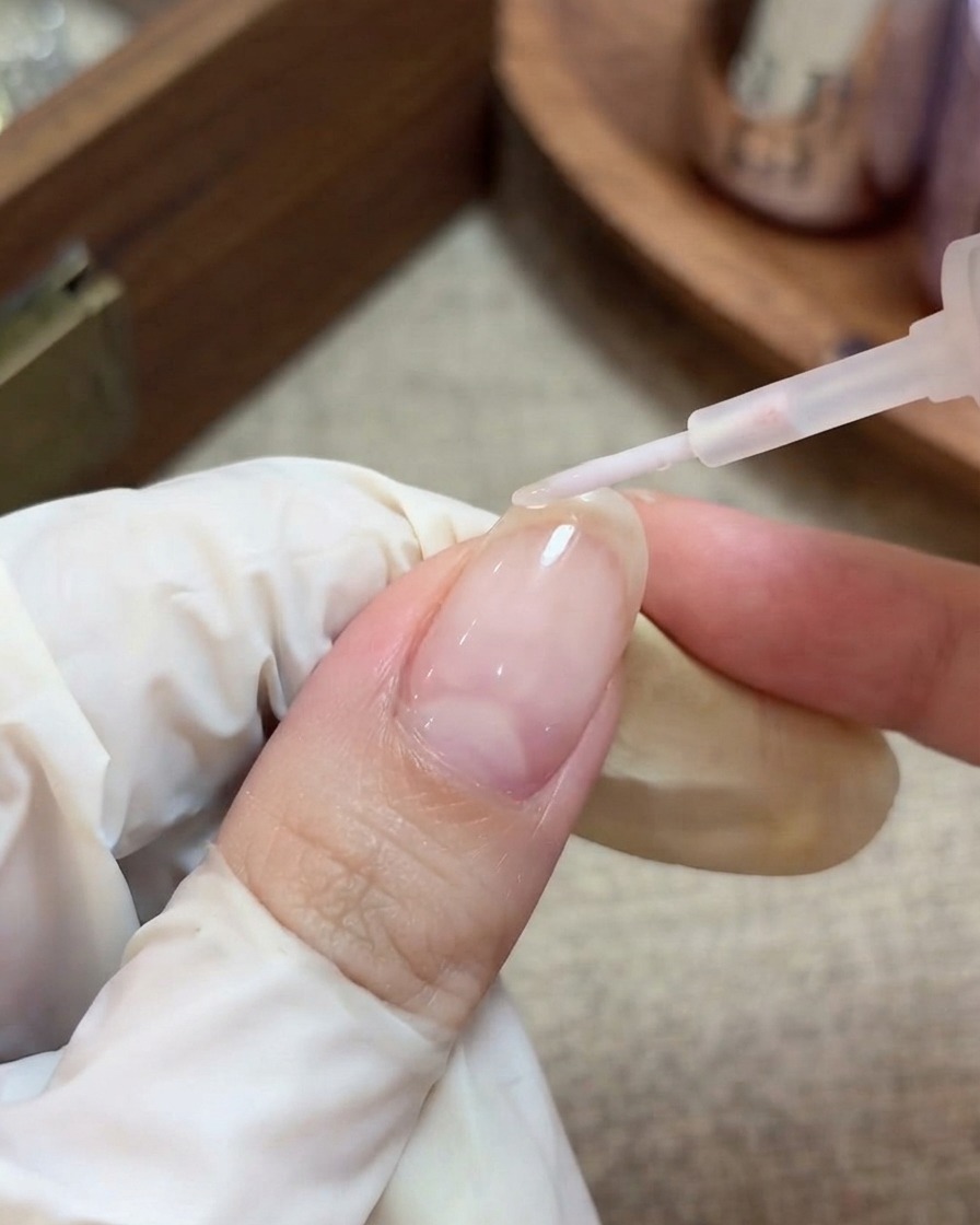 Una mano con guante usando un pincel para aplicar un top coat transparente y brillante sobre una uña con estrellas encapsuladas.