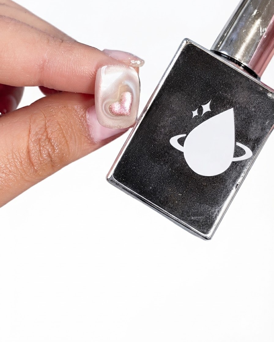 Una uña preparada junto a un frasco negro de capa superior con un logotipo de planeta blanco y una gota.