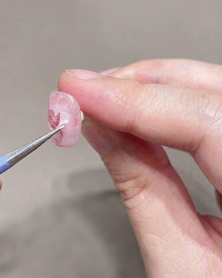 Un pincel fino aplicando una segunda capa de esmalte en gel rosa muy claro sobre la uña preparada.