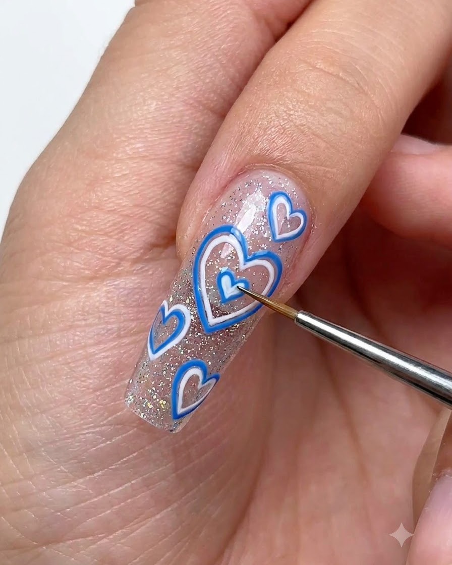 Un pincel fino para detalles usando gel de dibujo blanco para delinear pequeños corazones con volumen sobre una uña extendida brillante.