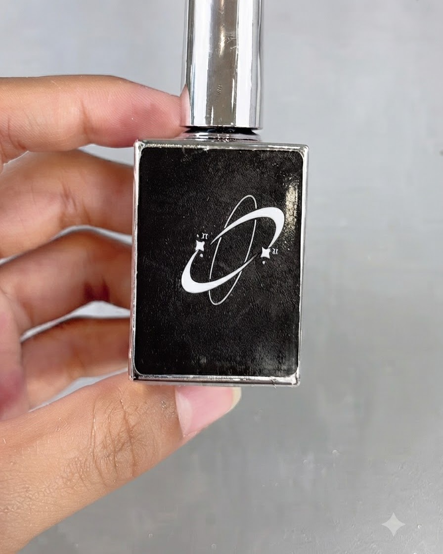 Una botella de cosméticos negra con un logotipo gráfico de planeta sostenida en la mano.
