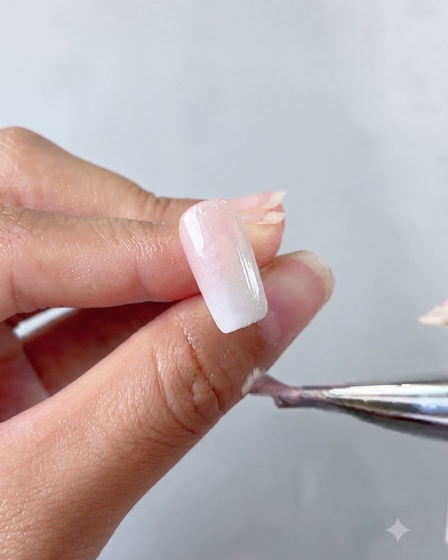Una mano sosteniendo un pincel que aplica una capa base de gel ojo de gato blanco lechoso sobre una uña.