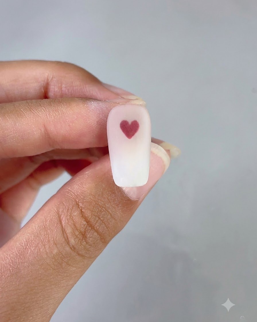 Una uña terminada que muestra un fondo ordenado de degradado rosa y blanco con un corazón rojo limpio en el centro.