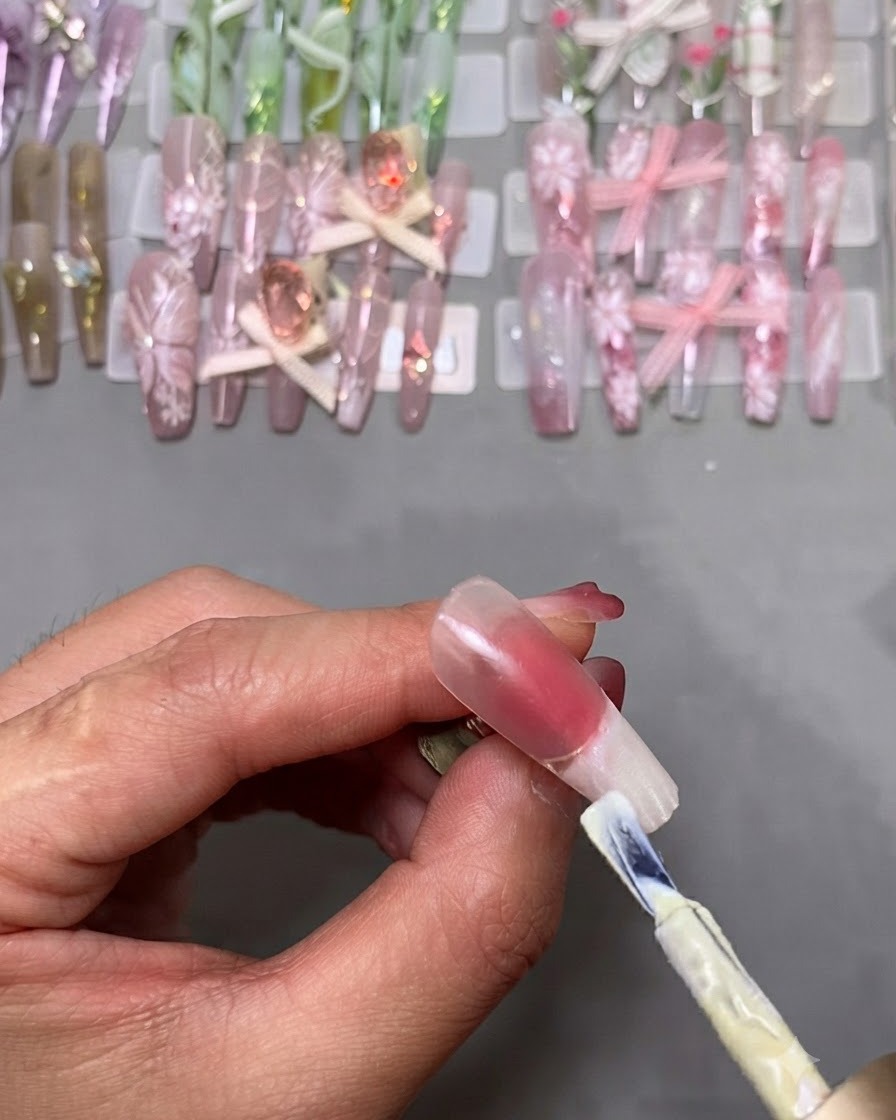 Un pincel de esmalte en gel aplicando esmalte blanco en la punta de una uña postiza montada en un soporte.