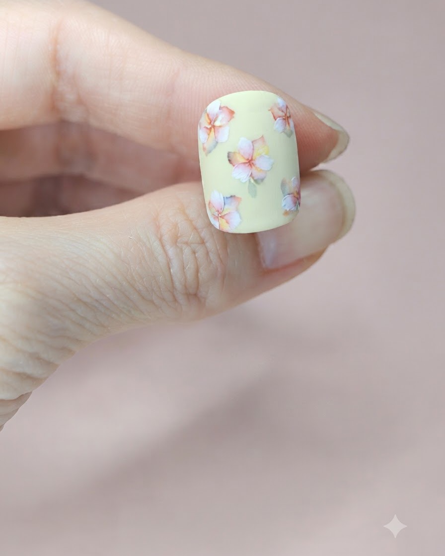 Primer plano de una uña amarilla mostrando una pequeña hoja de acuarela verde pintada junto al diseño floral central.