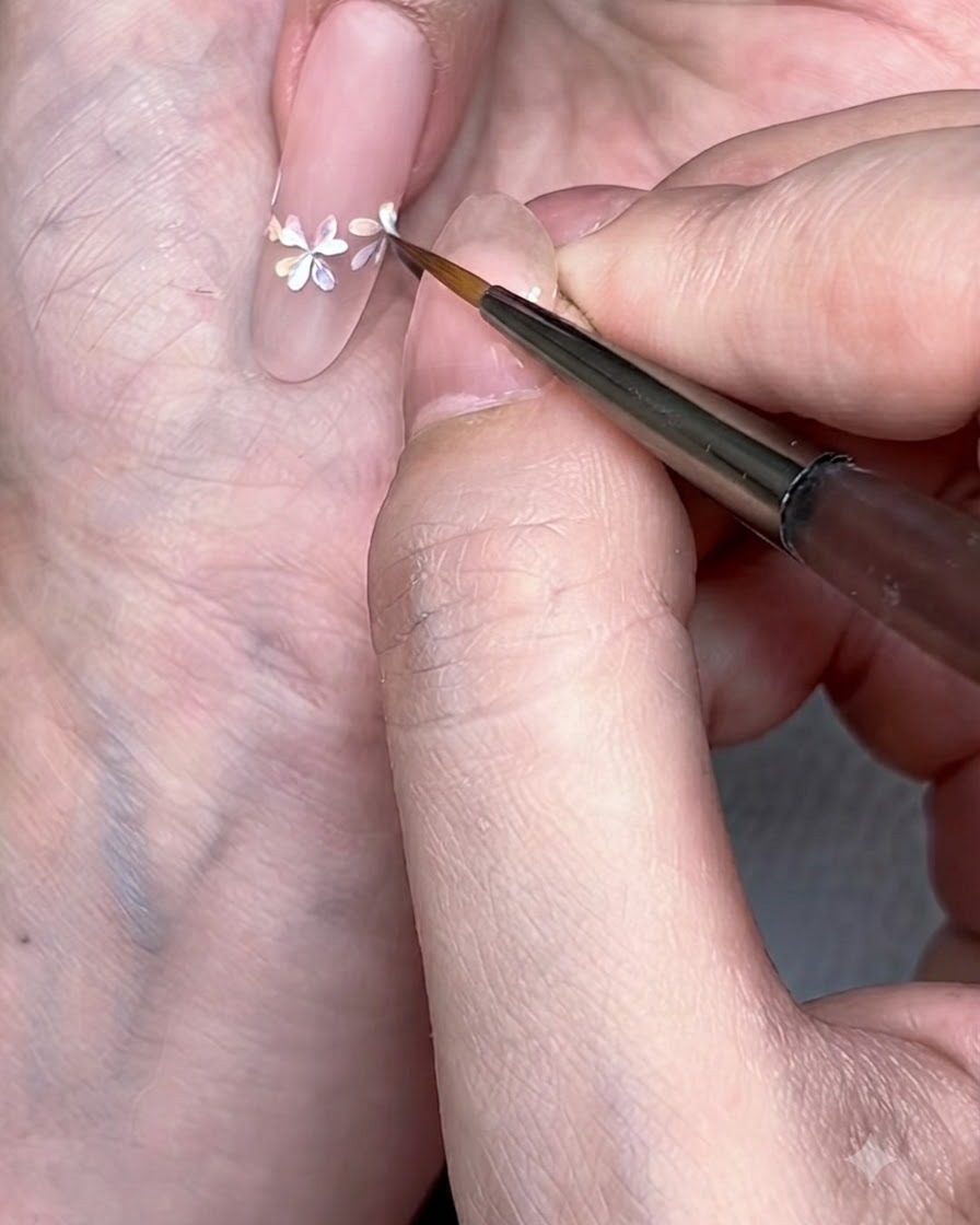 Primer plano detallado de un pincel liner añadiendo pétalos blancos nítidos sobre los centros florales en acuarela.