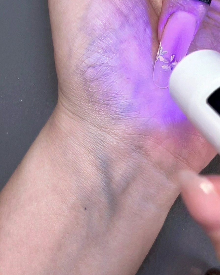 Mini lámpara UV de mano curando un diseño de uñas floral bajo luz morada.