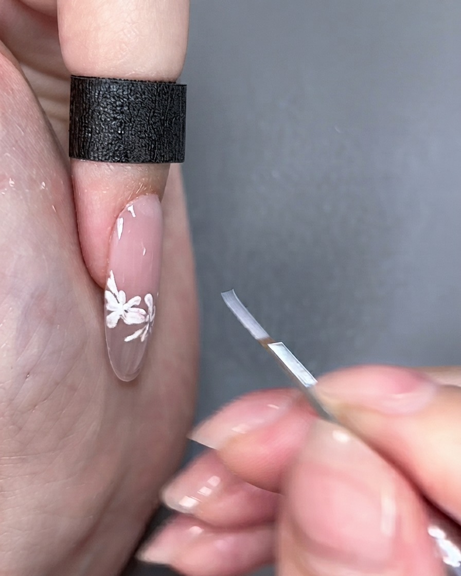 Pincel de nail art sostenido junto a una uña terminada bajo iluminación de estudio.