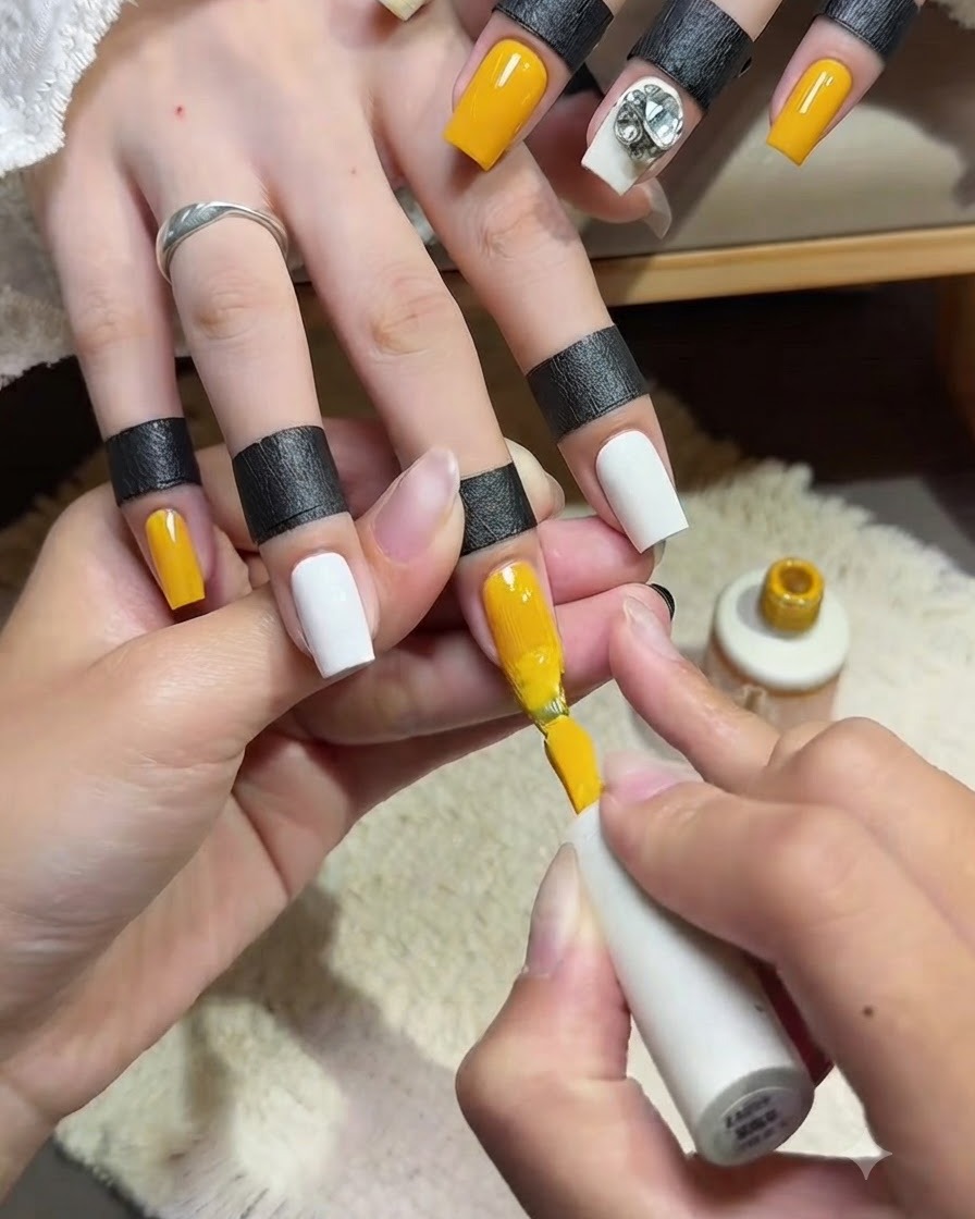 Primer plano de un técnico de uñas aplicando una segunda capa uniforme de esmalte en gel amarillo brillante en la uña del dedo índice con la brocha.