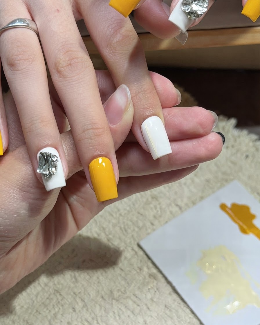 Un pincel de nail art aplicando una segunda línea amarilla horizontal muy fina sobre una uña blanca.