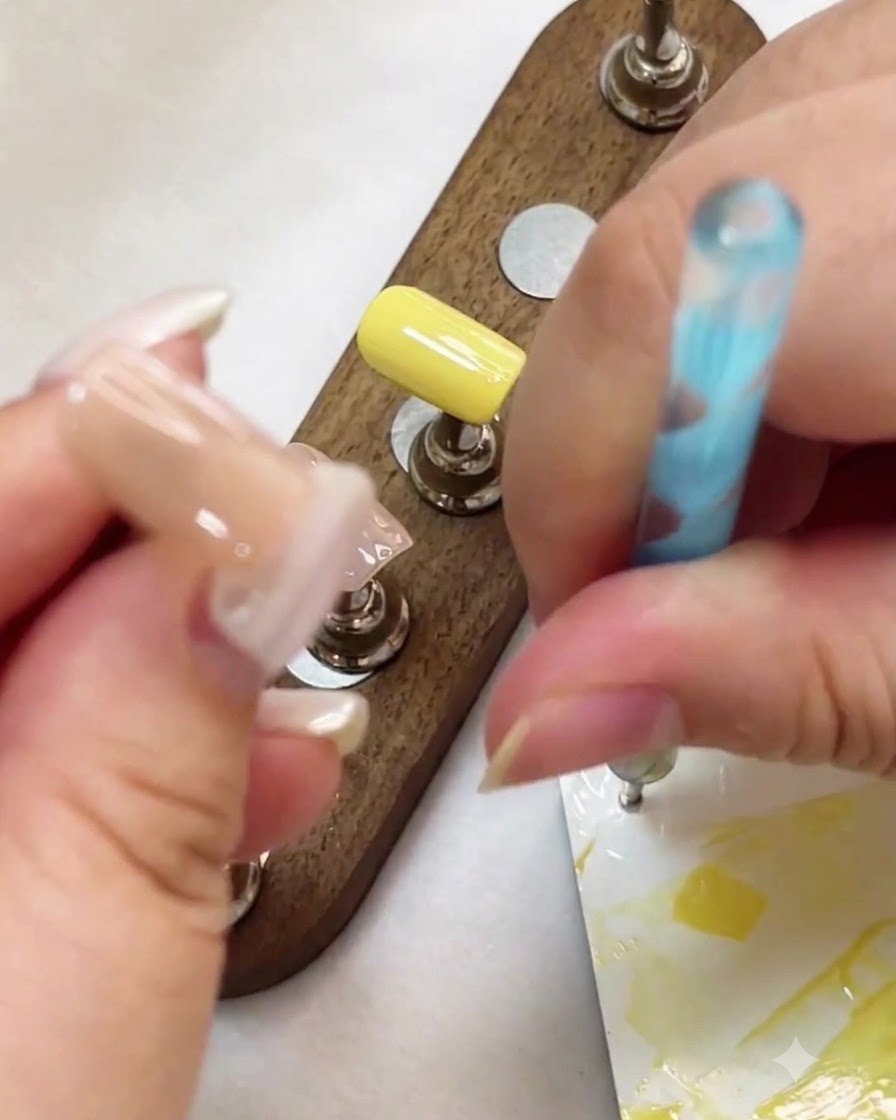 Un puntero dotting utilizado para colocar puntos de gel blanco sobre la superficie de una uña en tono nude.