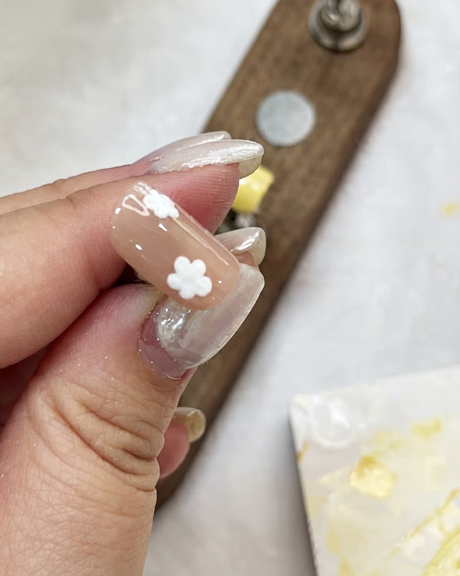 Una mano sosteniendo un tip de uña color nude mientras añade puntos blancos para crear el diseño floral.