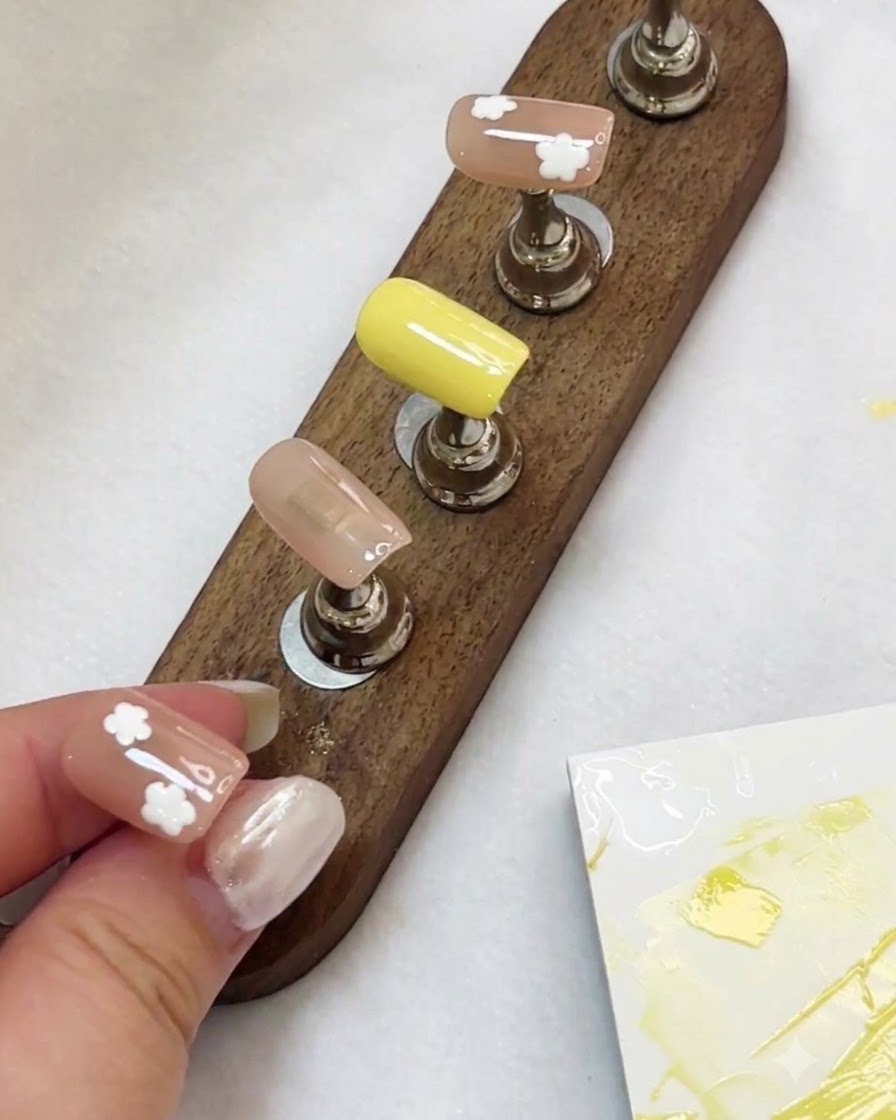 Un soporte con múltiples uñas postizas decoradas con diseños de flores blancas bajo la luz de una lámpara UV/LED.