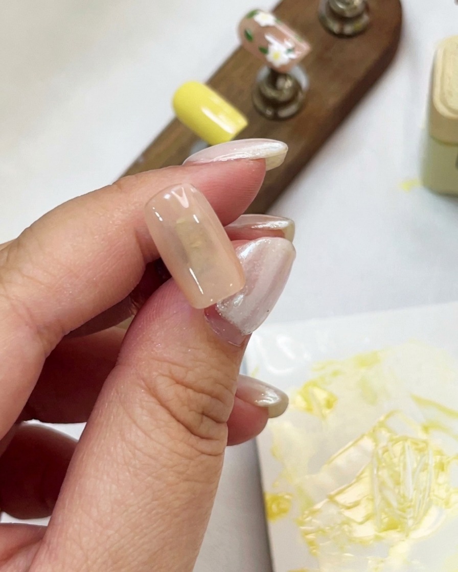 Un primer plano de una mano sosteniendo un tip color nude mientras aplica gel ojo de gato brillante con un pincel.
