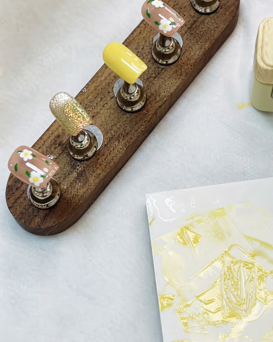 Un soporte de madera sosteniendo las uñas florales y la uña con efecto ojo de gato sobre una mesa.