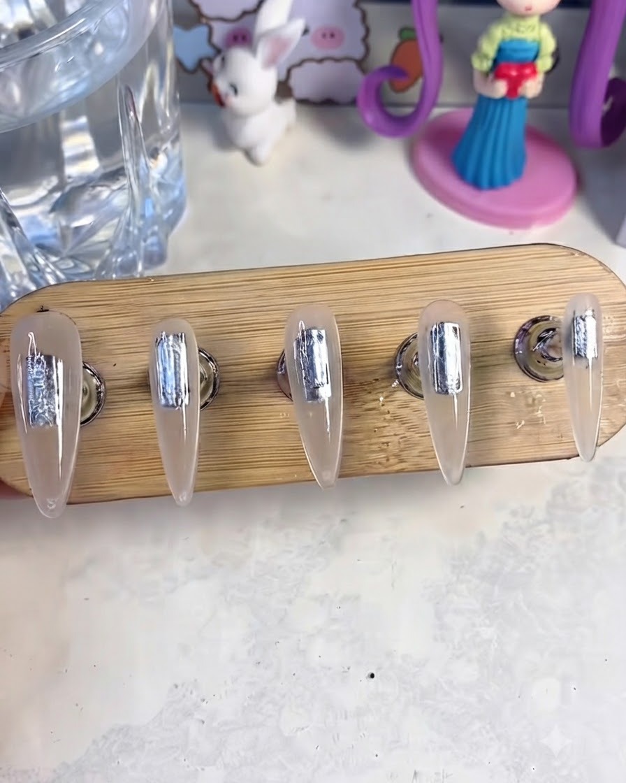 Un soporte para uñas con cinco uñas postizas colocadas dentro de una lámpara de curado UV y LED para curar la capa de gel base.