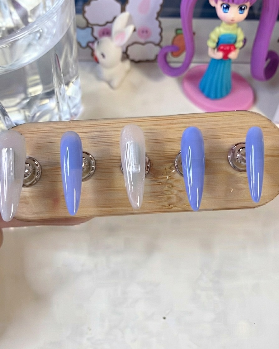 Un soporte para uñas que muestra uñas pintadas en azul y blanco lechoso curándose bajo una lámpara UV o LED.