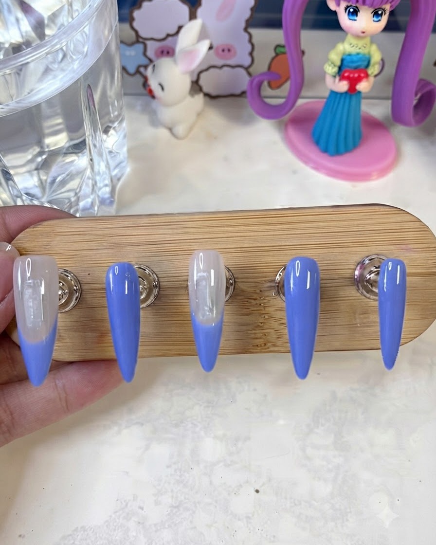 Un pincel de arte de uñas aplicando una segunda capa de pintura de punta francesa azul en los bordes de las uñas sobre un soporte de exposición.