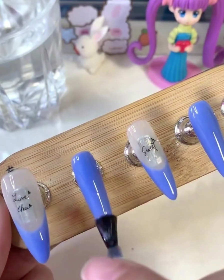 Un pincel aplicando una capa superior mate de manera uniforme a través de la superficie de las uñas pintadas en un soporte de madera.