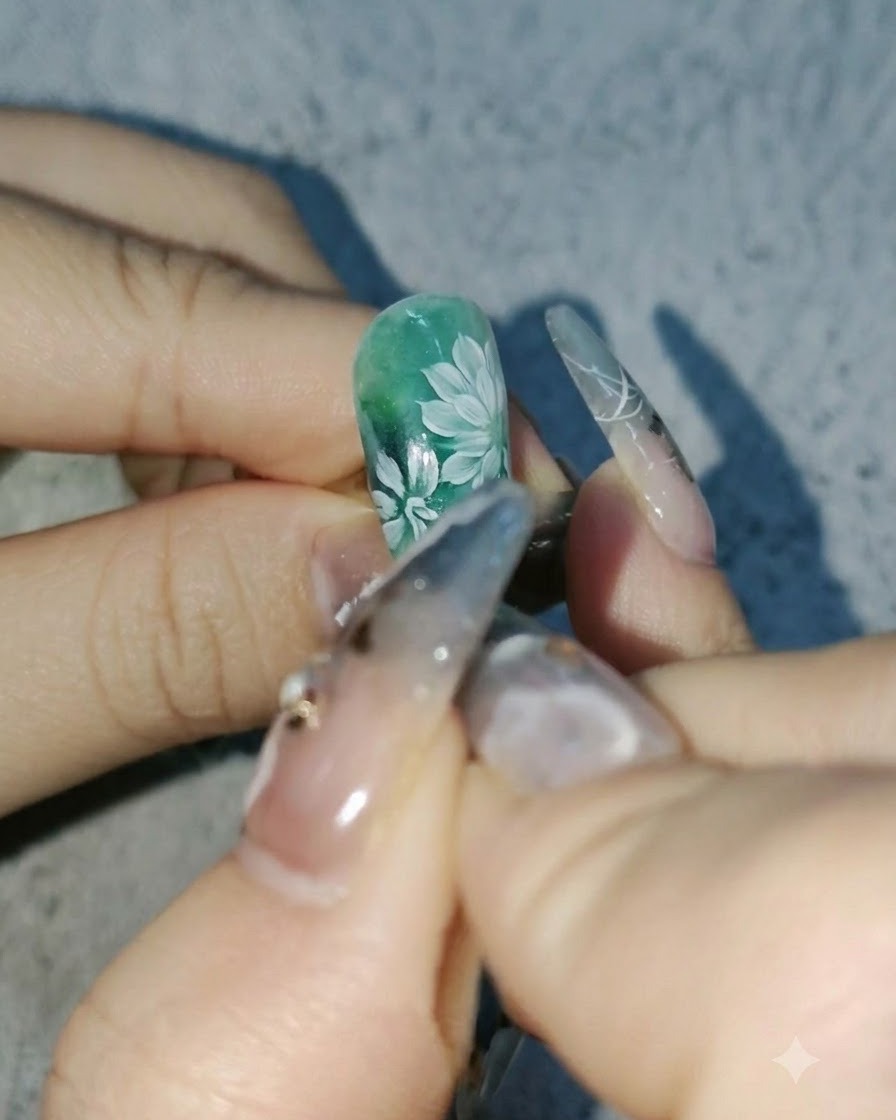 Una vista de cerca de una artista de uñas agregando pétalos blancos más profundos a las margaritas en un diseño verde.