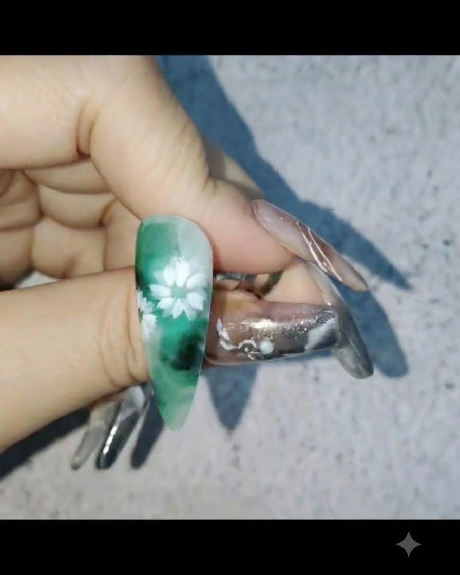 Una mano sosteniendo una uña con arte de margaritas blancas mientras aplica una capa protectora de gel reforzador.