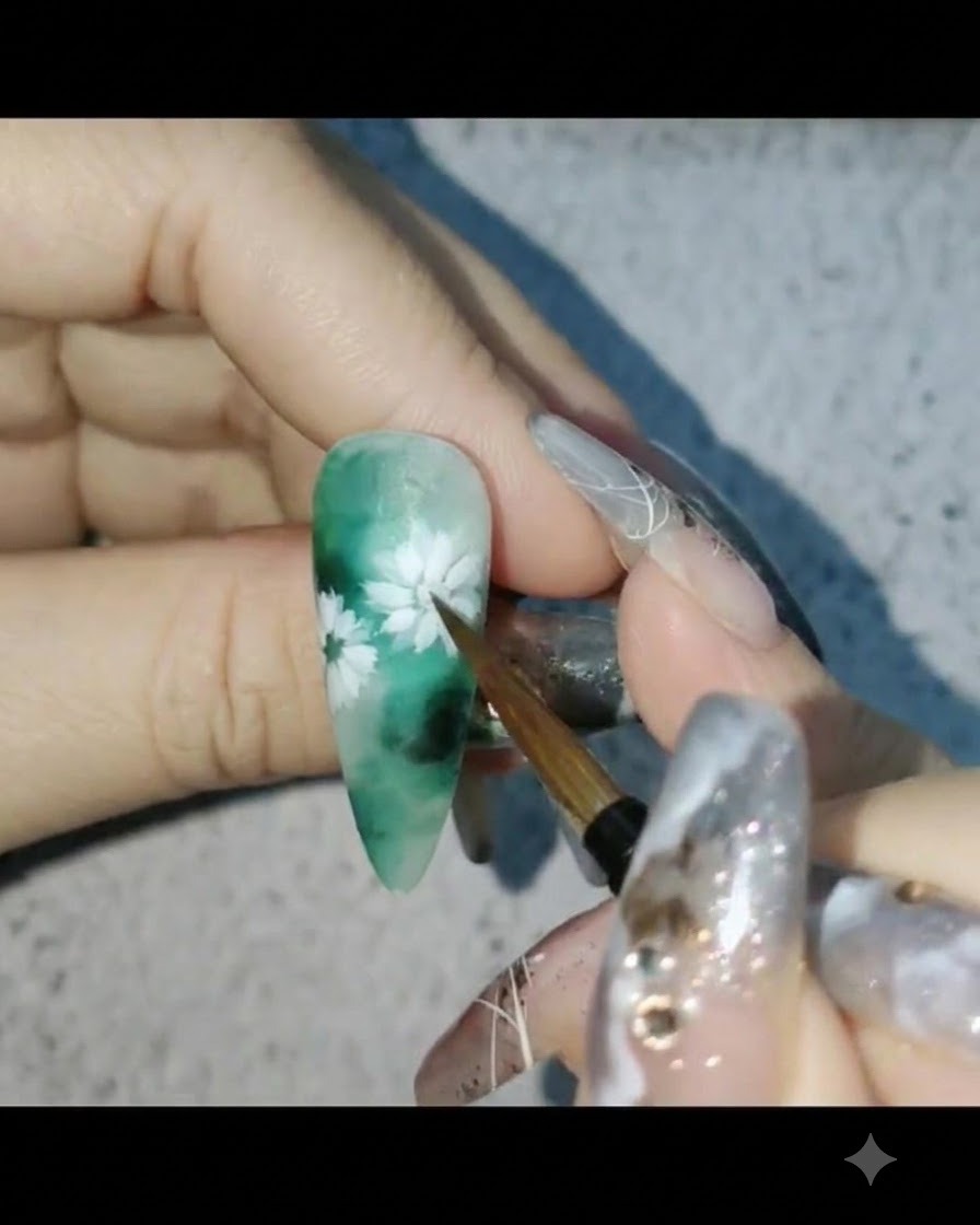 Un pincel de uñas aplicando top coat mate sobre un diseño de uñas floral de temática verde.
