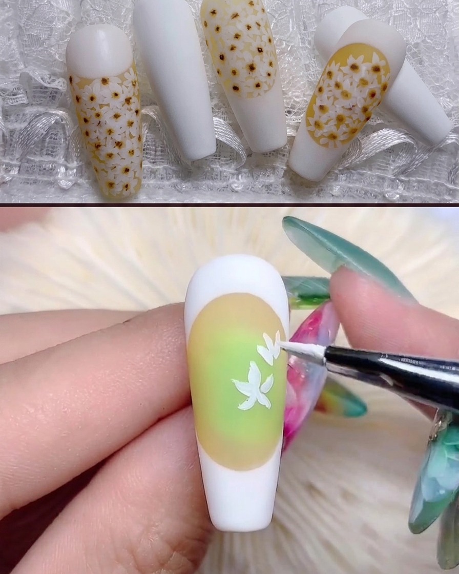Un pincel fino pintando formas de pétalos de margaritas blancas sobre la uña de tono amarillo.