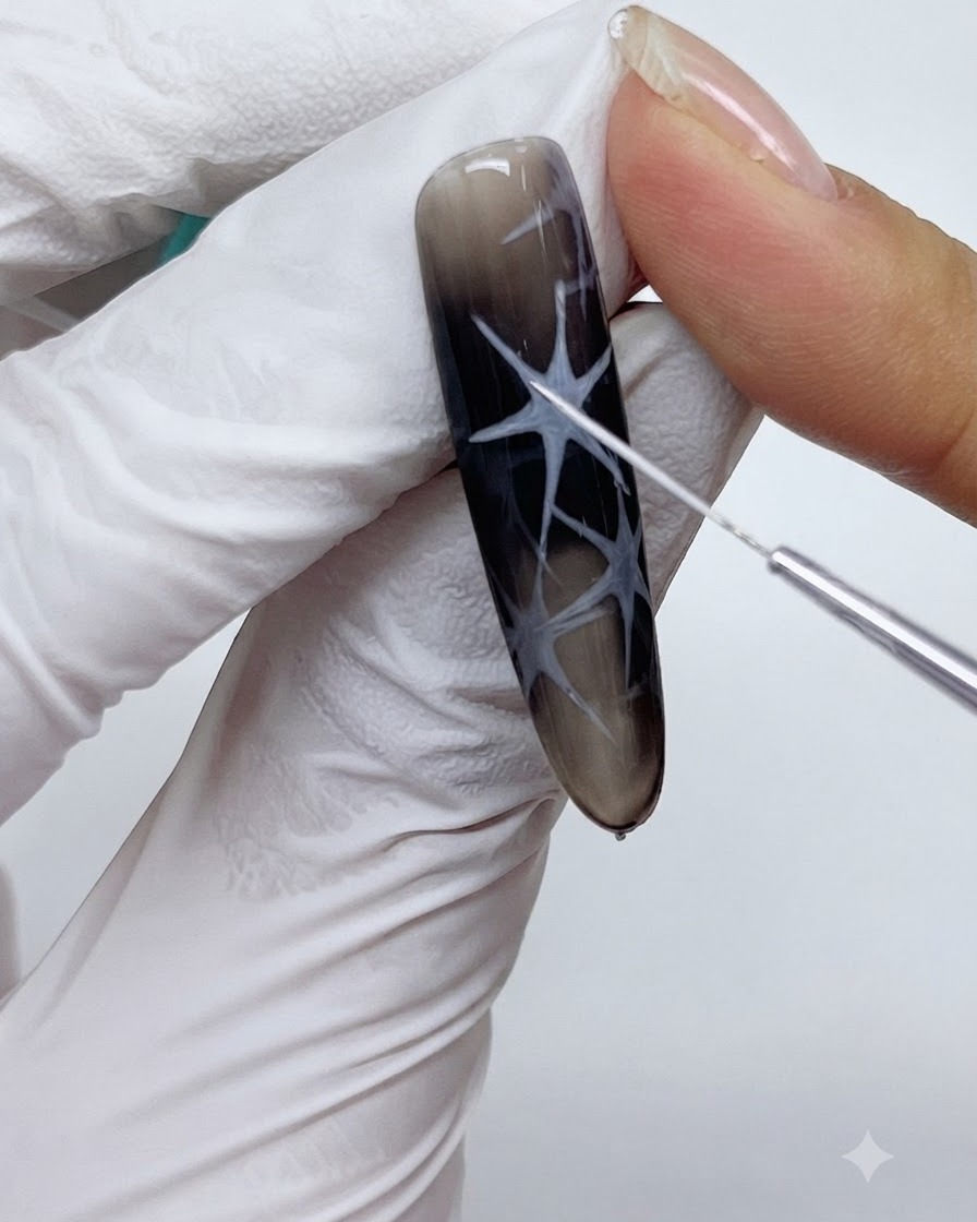 Una vista de primer plano de un pincel delineador fino dibujando delicadas líneas blancas dentro de un diseño de arte de uñas de estrella.