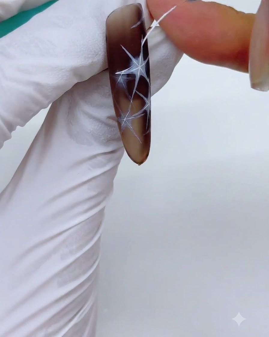 Una uña con diseños de estrellas blancas delineadas siendo colocada en una lámpara UV/LED para curar.