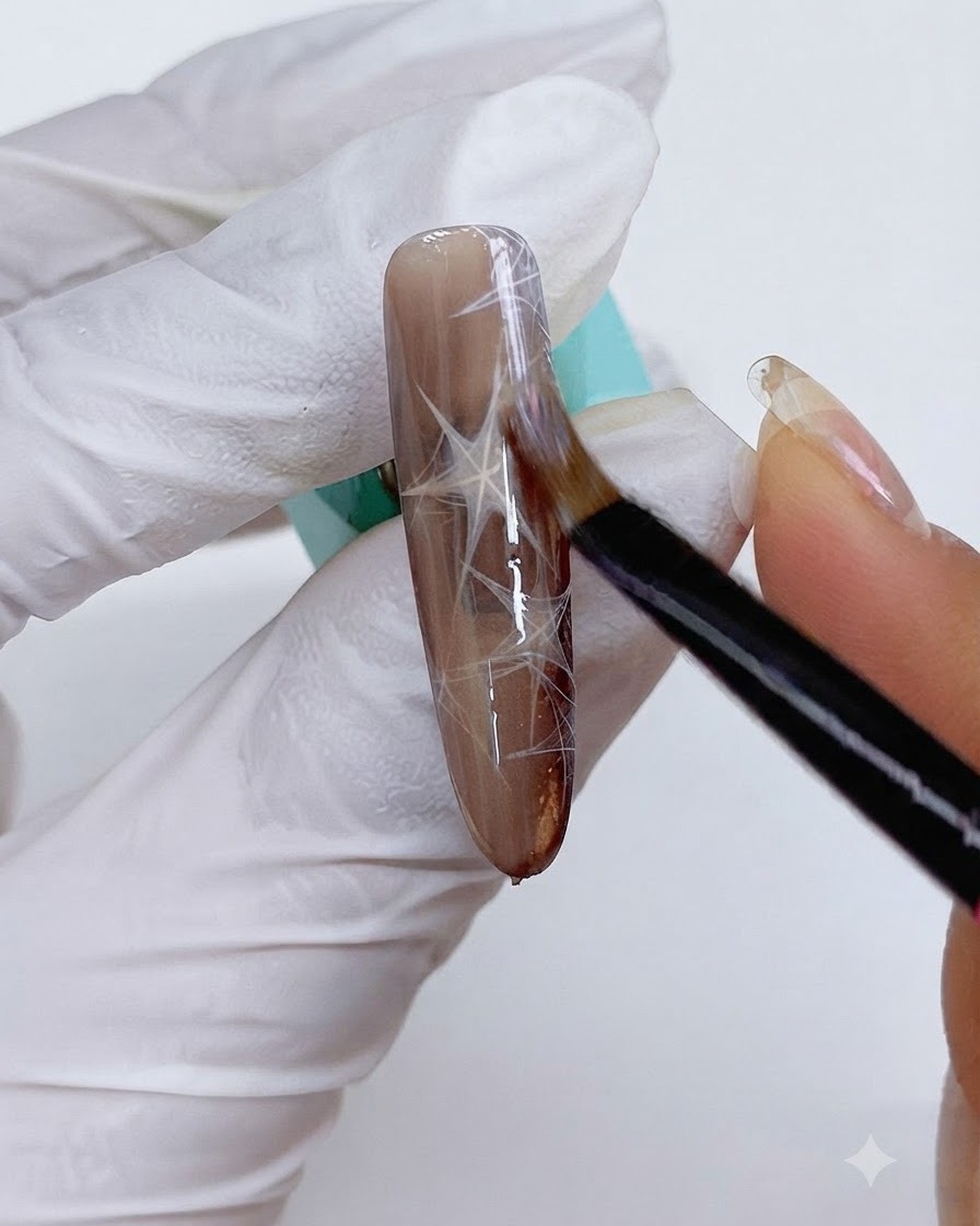 Un pincel fino aplicando gel cat-eye sobre la uña marrón decorada.