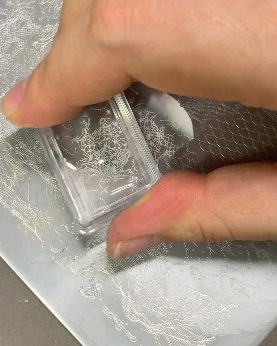 Un estampador transparente transfiriendo un patrón de encaje blanco sobre una uña transparente.