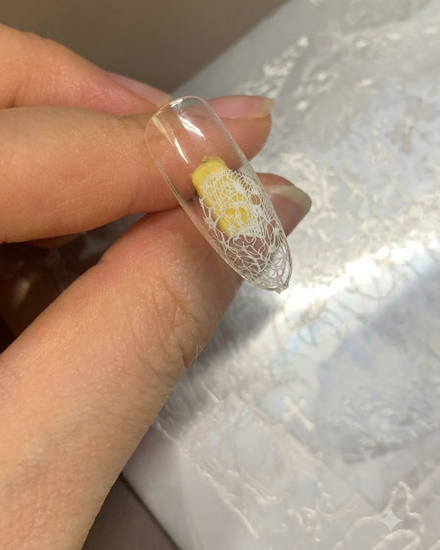 Una punta de uña que muestra un patrón de encaje blanco transferido en el borde y una base de gel beige en el resto.