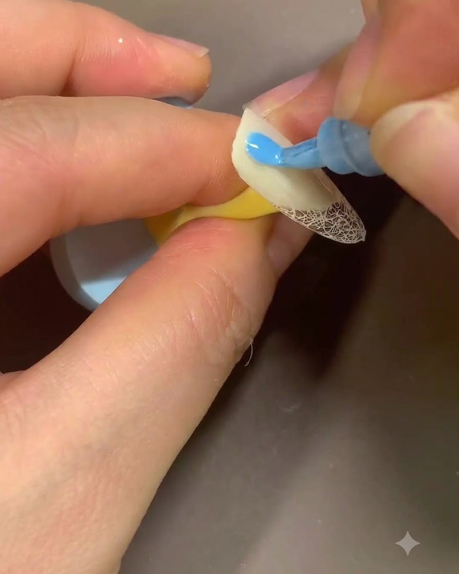 Un marcador azul dibujando pequeñas formas de pétalos de flor sobre la superficie beige de una uña.