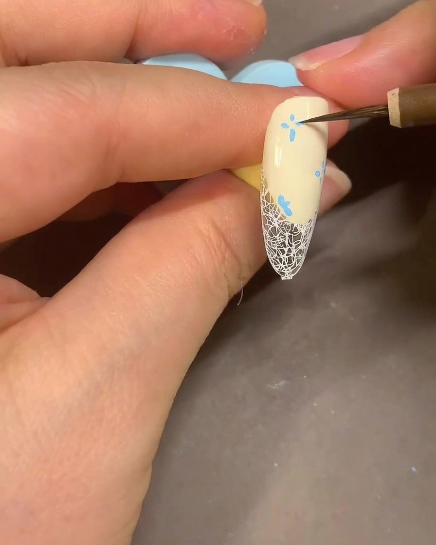 Un pincel de acuarela difuminando pétalos de flores con marcador azul en una uña con alcohol para un aspecto ahumado.