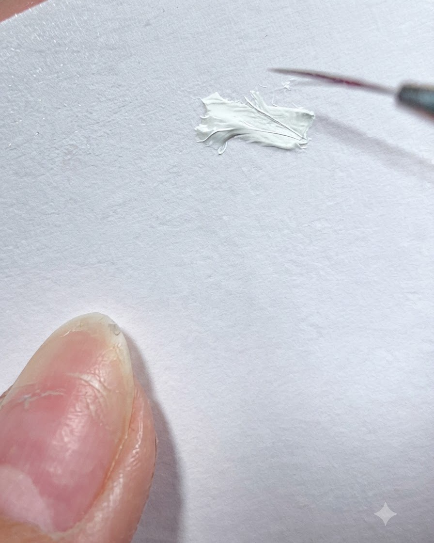 Un pincel liner fino tomando pintura de gel blanco de una paleta de superficie blanca.