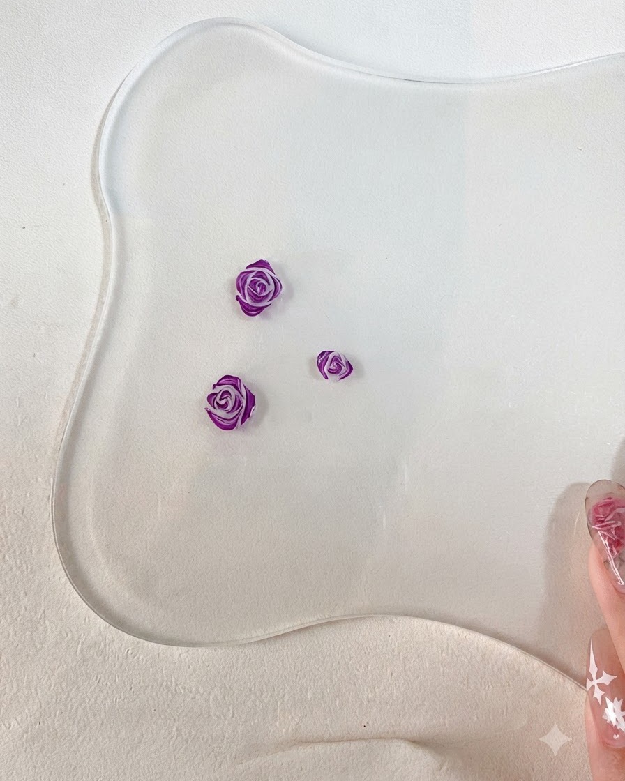 Un primer plano de un pincel de arte de uñas fino añadiendo contornos detallados de color morado oscuro a los bordes de los pétalos de rosa esculpidos en 3D.